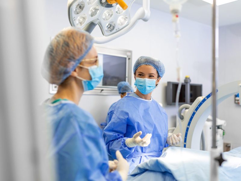 Female surgeon with surgical mask at operating room. Young woman doctor in surgical uniform in hospital operation theater.