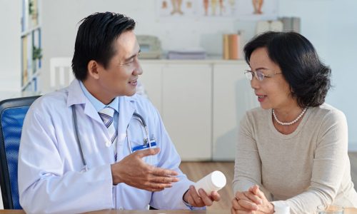Wait-up portrait of friendly doctor sitting at desk and prescribing drugs to pretty senior patient